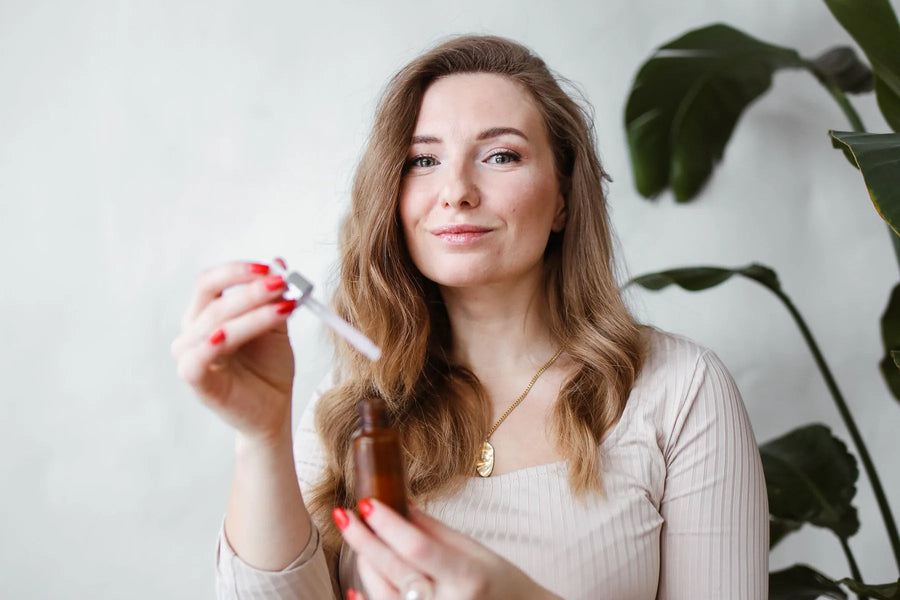 Woman holding a facial serum dropper beside indoor plants