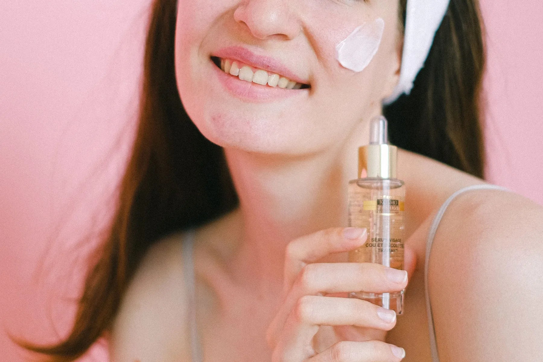 Woman applying skincare against a soft pink background