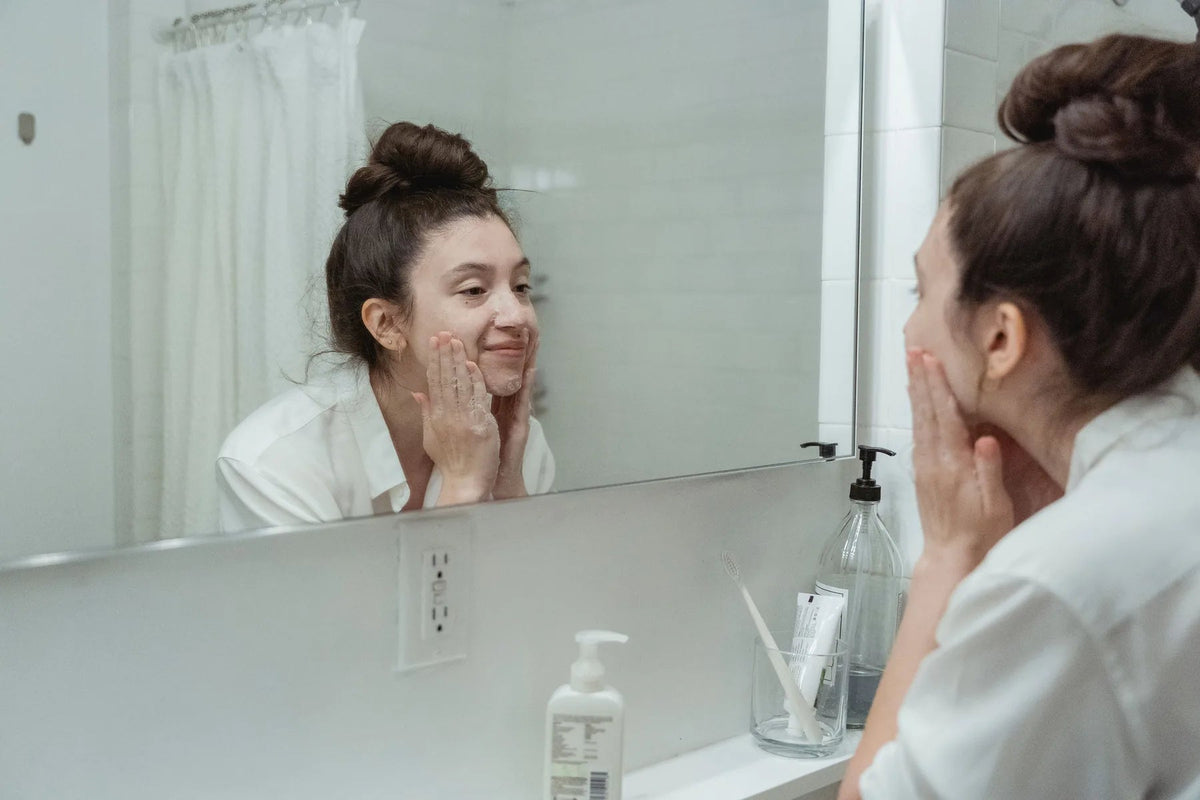 Woman applying skincare while looking in a bathroom mirror