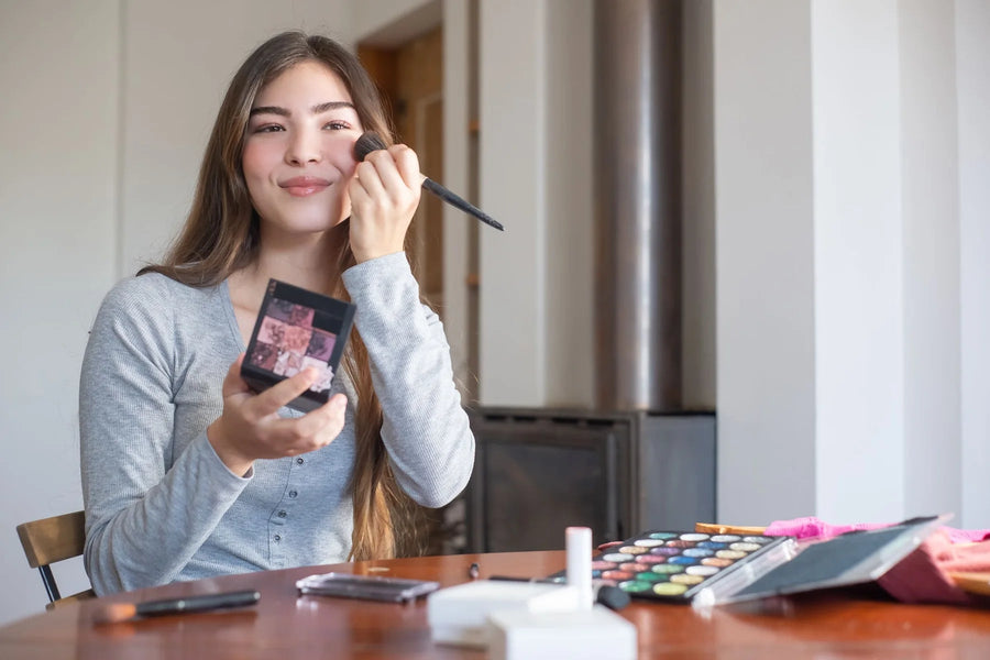 Woman applying blush to her cheek with a makeup brush in natural light