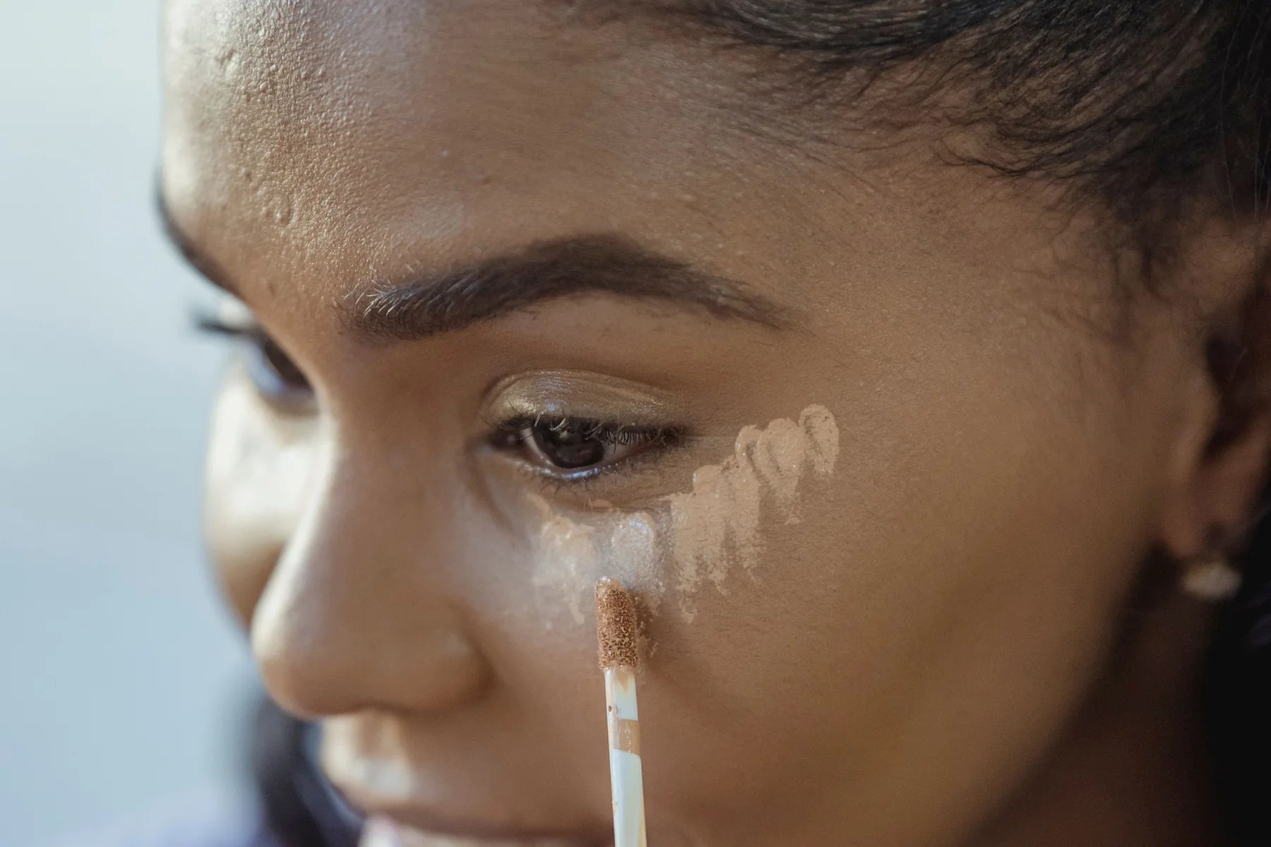 Woman applying concealer beneath her eye in natural light