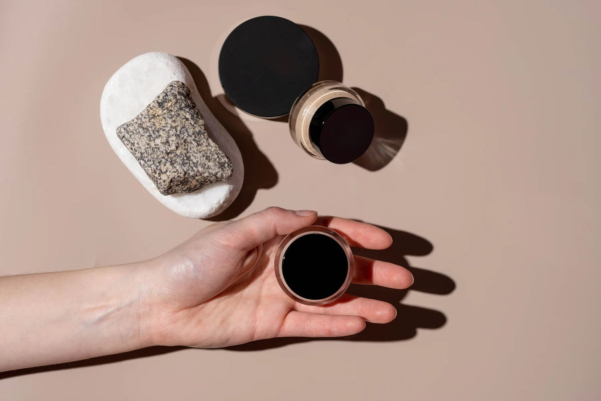 Hand inspecting an open makeup container beside cosmetic products