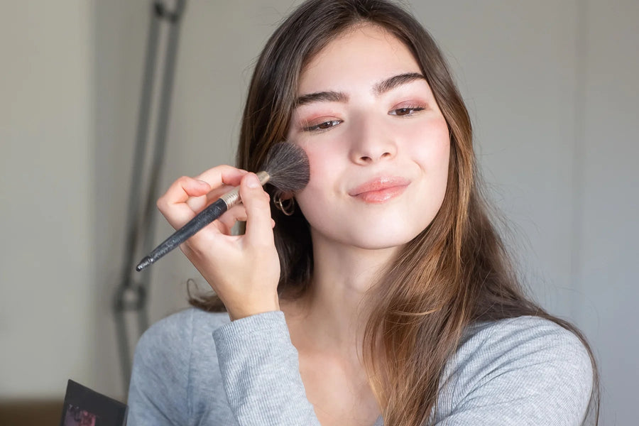 Woman applying face makeup with a brush in natural light