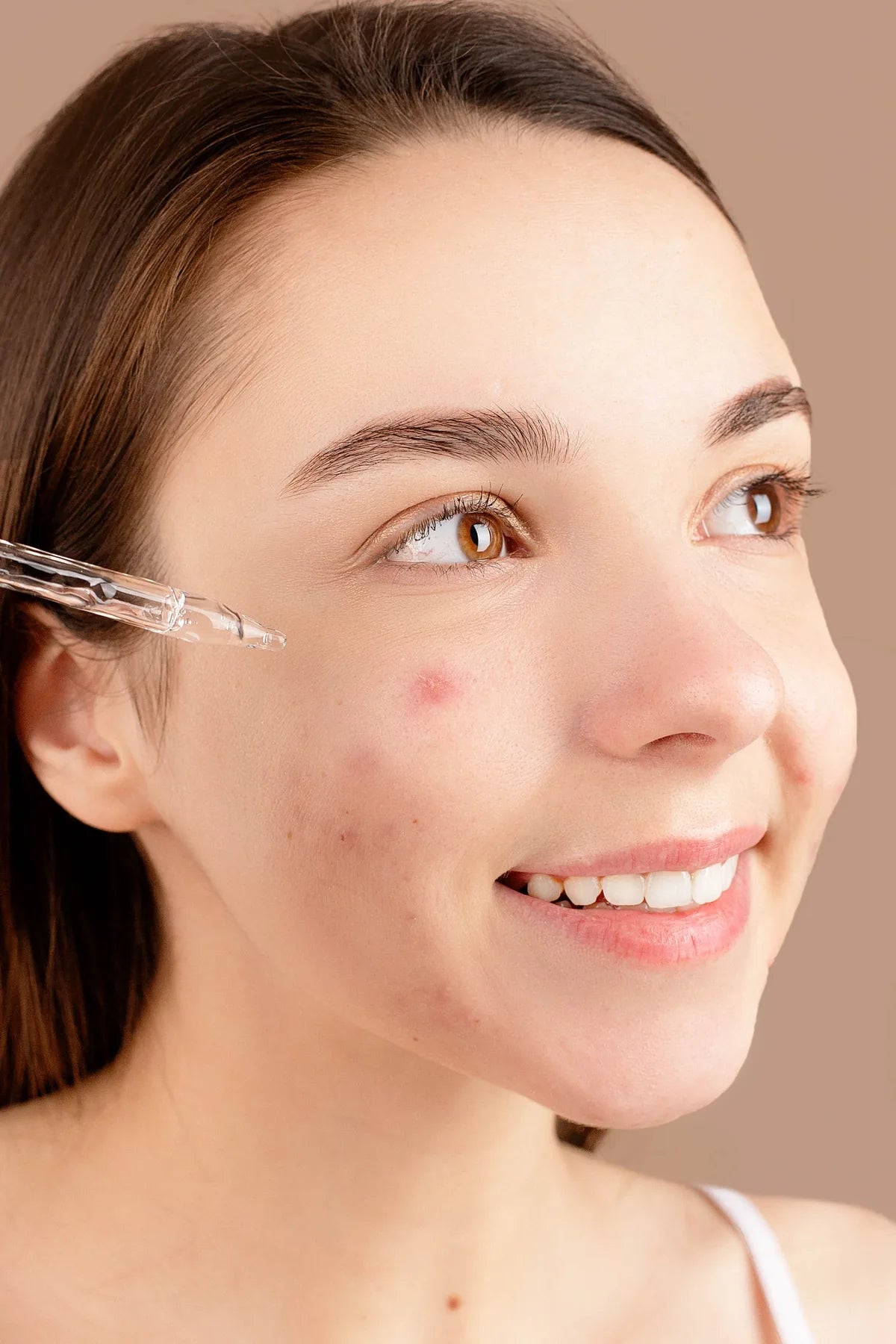 Woman applying face serum beside a visible blemish