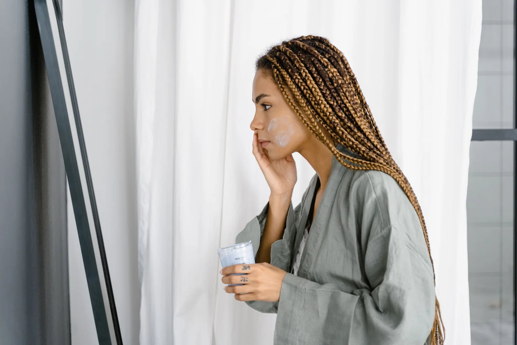 Woman applying facial moisturizer while looking in a mirror