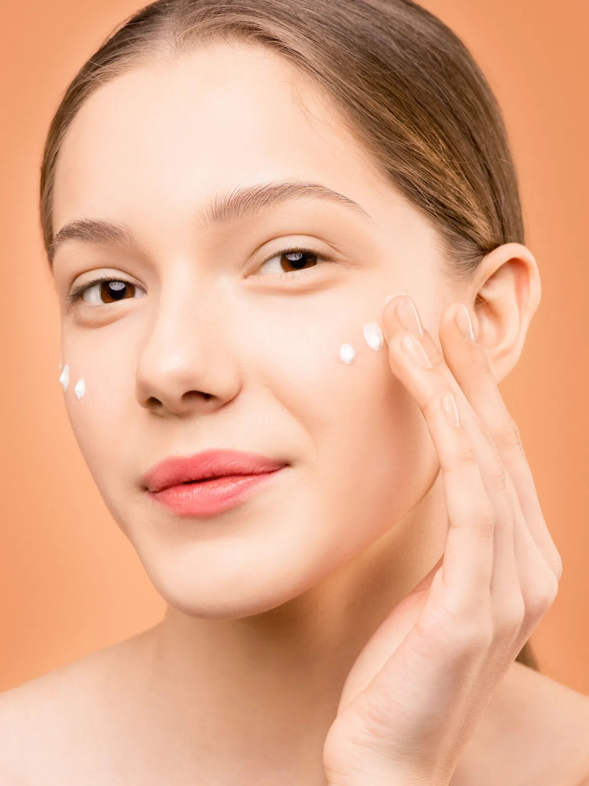 Woman applying small dots of face cream to her cheek
