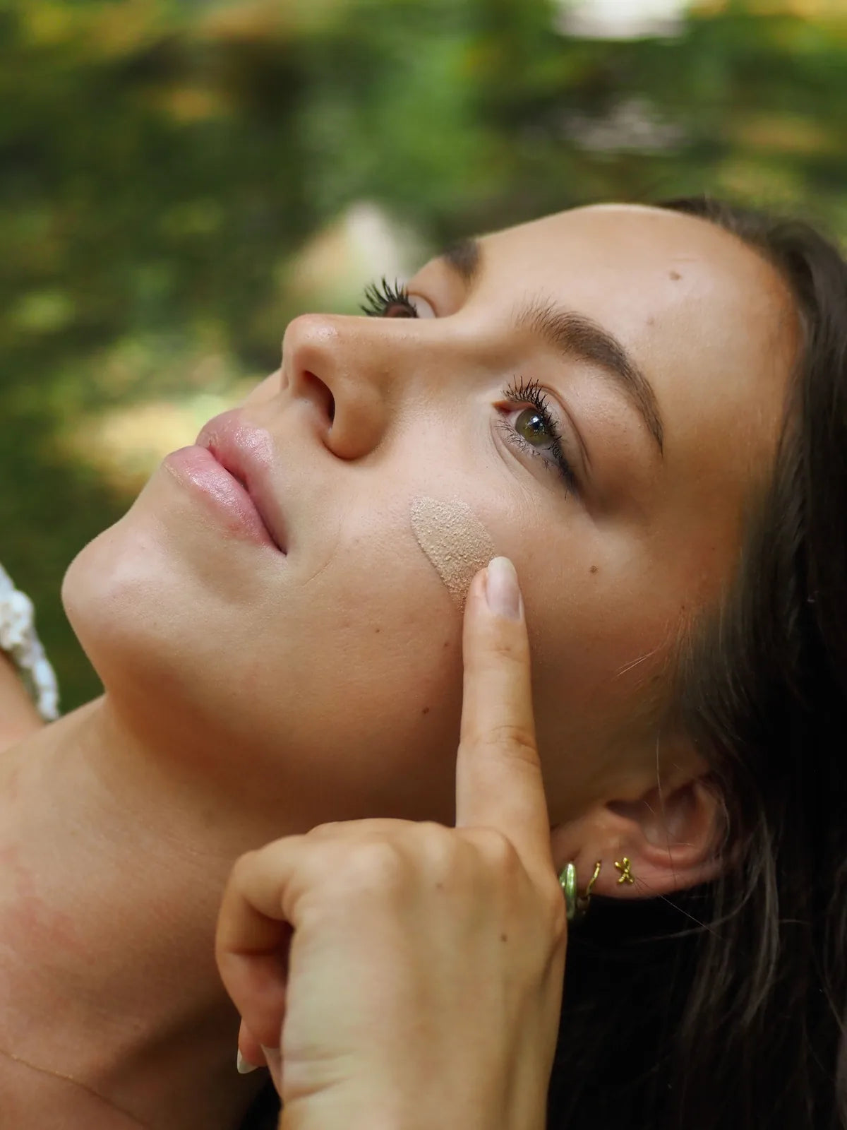 Woman applying a tinted skincare cream to her cheek outdoors