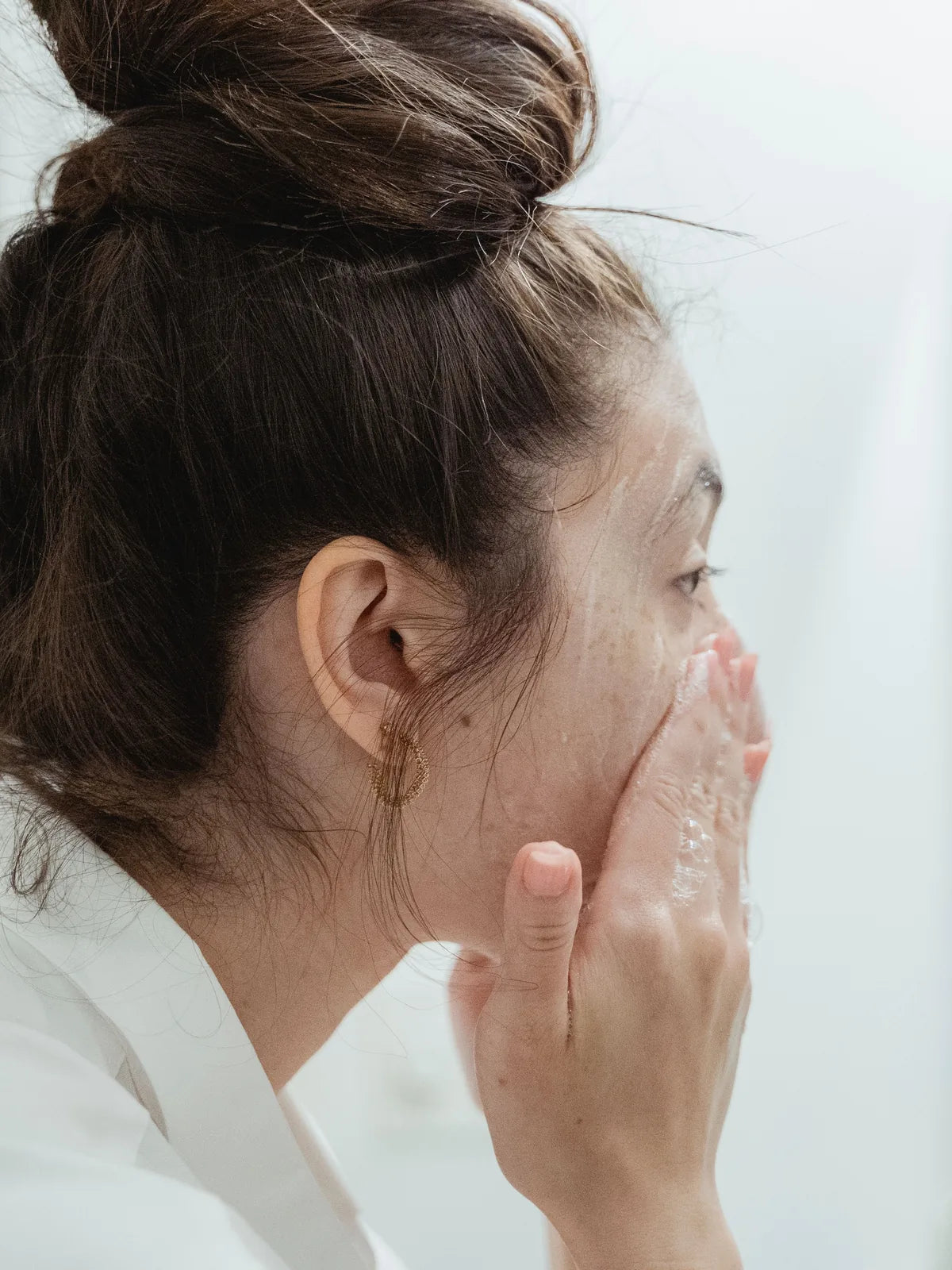 Woman gently washing her face with water at a bathroom sink